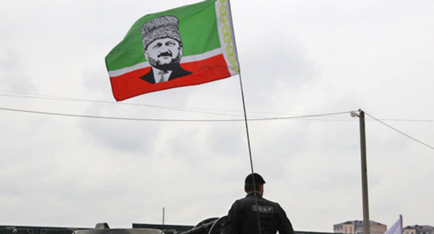 An officer of the Chechen Special Rapid Response Unit (SOBR) with a flag of the Republic with a portrait of Akhmat Kadyrov. May 9, 2015. Grozny. Photo by Magomed Magomedov for the "Caucasian Knot" An officer of the Chechen Special Rapid Response Unit (SOBR) with a flag of the Republic with a portrait of Akhmat Kadyrov. May 9, 2015. Grozny. Photo by Magomed Magomedov for the "Caucasian Knot"