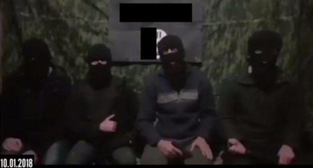 Four masked men sitting at the background of the IS'* flag call on their followers to kill Russian rights defenders. Screenshot of the video. Four masked men sitting at the background of the IS'* flag call on their followers to kill Russian rights defenders. Screenshot of the video.