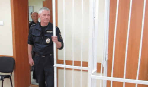 A law enforcer at the cage in courtroom. Screenshot of a video "Berdsk Online" https://www.youtube.com/watch?v=-W8kL4as5N0 A law enforcer at the cage in courtroom. Screenshot of a video "Berdsk Online" https://www.youtube.com/watch?v=-W8kL4as5N0