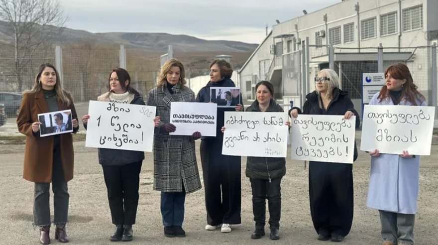 Participants of the action with posters in support of Mzia Amaglobeli. Screenshot of the photo "Interpressnews" from 11.01.26, https://www.interpressnews.ge/ru/article/172626-v-znak-solidarnosti-s-mziei-amaglobeli-zhenshchiny-politiki-sobralis-u-zdaniia-rustavskoi-zhenskoi-kolonii.