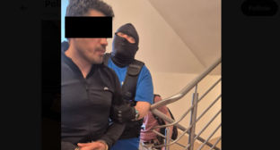 A security officer leads Elnur A. Screenshot of a Lublin police photo from 20.06.26, https://x.com/PolicjaLubelska/status/2068301027225292818/photo/1.